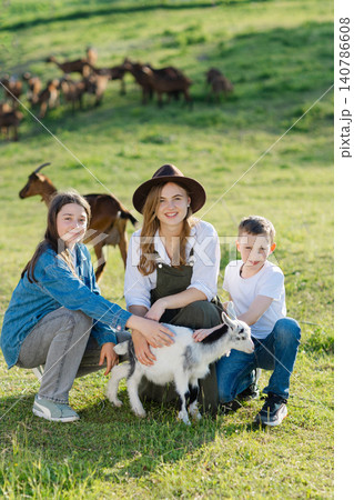 Farmers petting a baby goat in green field with goats in background 140786608