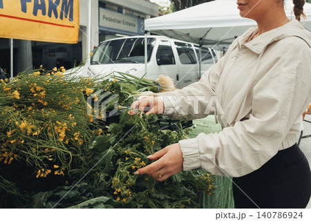Woman selects fresh herbs at vibrant market stall Woman selects fresh herbs at vibrant market stall 140786924