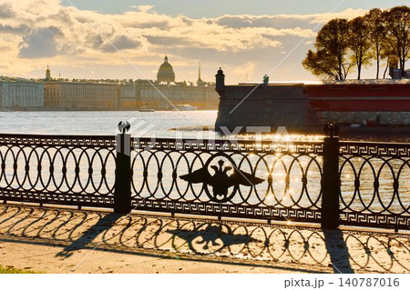 Isaac cathedral, Winter Palace, picturesque metal railings with a double-headed eagle and the crown of the Russian Empire on embankment in St. Petersburg, autumn sunset, incredible sun glare, Russia Isaac cathedral, Winter Palace, picturesque metal railings with a double-headed eagle and the crown of the Russian Empire on embankment in St. Petersburg, autumn sunset, incredible sun glare, Russia 140787016