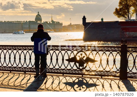 Isaac cathedral, Winter Palace, picturesque metal railings with a double-headed eagle and the crown of the Russian Empire on embankment in St. Petersburg, autumn sunset, incredible sun glare, Russia Isaac cathedral, Winter Palace, picturesque metal railings with a double-headed eagle and the crown of the Russian Empire on embankment in St. Petersburg, autumn sunset, incredible sun glare, Russia 140787020