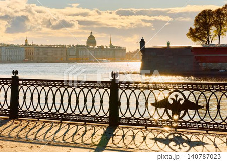 Isaac cathedral, Winter Palace, picturesque metal railings with a double-headed eagle and the crown of the Russian Empire on embankment in St. Petersburg, autumn sunset, incredible sun glare, Russia 140787023