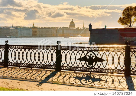 Isaac cathedral, Winter Palace, picturesque metal railings with a double-headed eagle and the crown of the Russian Empire on embankment in St. Petersburg, autumn sunset, incredible sun glare, Russia 140787024