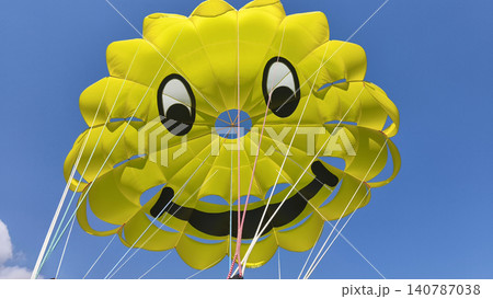 bright yellow smiley face parasailing canopy against a clear blue sky, fun, adventure and excitement of a sunny beach holiday and water sports activities. bright yellow smiley face parasailing canopy against a clear blue sky, fun, adventure and excitement of a sunny beach holiday and water sports activities. 140787038