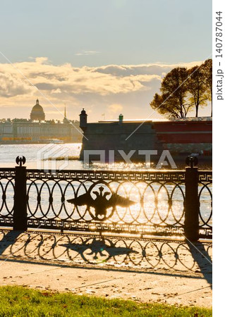 Isaac cathedral, Winter Palace, picturesque metal railings with a double-headed eagle and the crown of the Russian Empire on embankment in St. Petersburg, autumn sunset, incredible sun glare, Russia Isaac cathedral, Winter Palace, picturesque metal railings with a double-headed eagle and the crown of the Russian Empire on embankment in St. Petersburg, autumn sunset, incredible sun glare, Russia 140787044