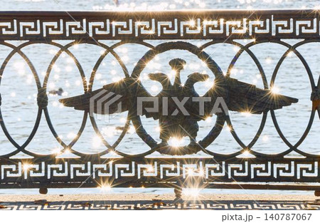 picturesque metal railings with a double-headed eagle and the crown of the Russian Empire on embankment in St. Petersburg, Russia, walking people, sunny autumn day, incredible sun glare Russia picturesque metal railings with a double-headed eagle and the crown of the Russian Empire on embankment in St. Petersburg, Russia, walking people, sunny autumn day, incredible sun glare Russia 140787067