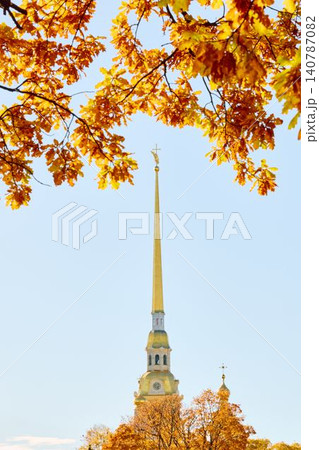 The golden spire of the Peter and Paul Fortress through yellow leaves in Saint-Petersburg - Russia at sunny autumn day, cross with angel on spire, red leaves, sunset, clear sky 140787082