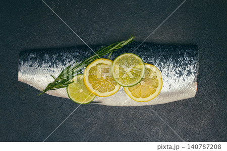 Fresh fish fillet, garnished with lemon and herbs, on a dark background, ready to cook 140787208