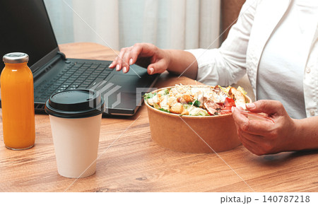 a woman is working on a laptop at home, there is food on the table, salad, coffee and juice, delivery, 140787218