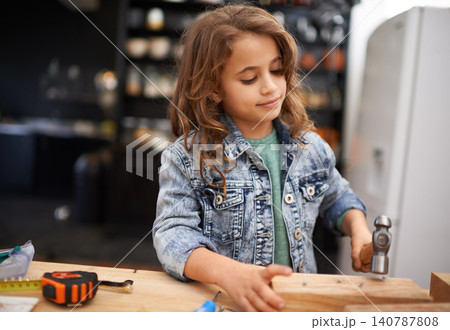 Girl, carpentry and hammer a nail in workshop, play and game in kitchen of home. Female person, child and equipment or tool for wood project or hobby, construction and remodeling or manufacture 140787808