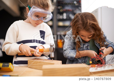 Children, construction and diy in workshop with tools, play and game in kitchen of home. Girls, hammer and safety glasses for wood project or building, carpentry and woodworking or manufacture Children, construction and diy in workshop with tools, play and game in kitchen of home. Girls, hammer and safety glasses for wood project or building, carpentry and woodworking or manufacture 140787809
