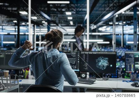 Engineer stretches at a workstation in a server hub to relieve back fatigue after long technical work. Engineer stretches at a workstation in a server hub to relieve back fatigue after long technical work. 140788665