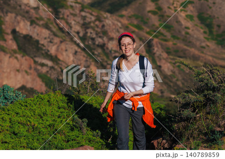 Young woman hiker with backpack walks along a mountain trail 140789859