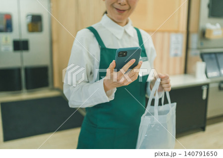 透明バッグからスマホを取り出してを見る50代女性スーパー店員の手元 140791650