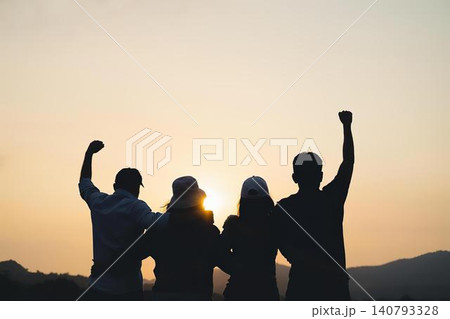 Group of four friends celebrating sunset outdoors with raised fists Group of four friends celebrating sunset outdoors with raised fists 140793328