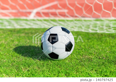 Classic Black and White Soccer Ball on Green Grass Pitch with Goal Net Background Classic Black and White Soccer Ball on Green Grass Pitch with Goal Net Background 140797425