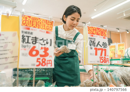 スーパーマーケットの青果担当の女性スタッフが価格POPに囲まれて商品を確認している スーパーマーケットの青果担当の女性スタッフが価格POPに囲まれて商品を確認している 140797566