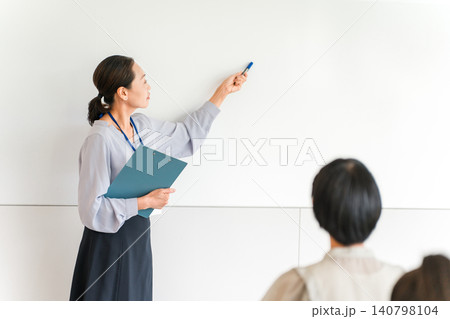 塾,セミナー,講習会でホワイトボードの前で講義する女性講師,教員,塾講師 140798104