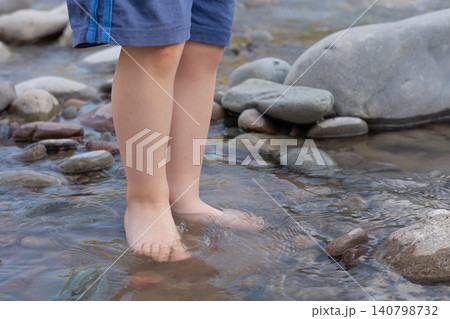 Close-up of a child's bare feet standing in clear river water on stones Close-up of a child's bare feet standing in clear river water on stones 140798732