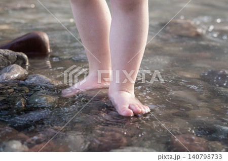 Close-up of a child's bare feet standing in clear river water on stones Close-up of a child's bare feet standing in clear river water on stones 140798733