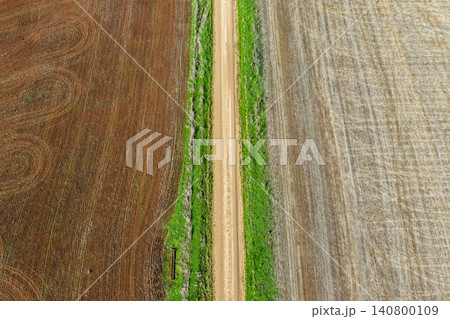 Aerial downward view of a green grass lined dirt road leading through cultivated agricultural fields, showcasing rural farmland patterns and textures beneath soft natural light in NSW, Australia. 140800109