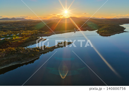 Aerial view showcasing the Lake Keepit dam wall and surrounding rural landscape at sunset, with warm golden light illuminating the reservoir and engineering infrastructure in NSW, Australia. Aerial view showcasing the Lake Keepit dam wall and surrounding rural landscape at sunset, with warm golden light illuminating the reservoir and engineering infrastructure in NSW, Australia. 140800756