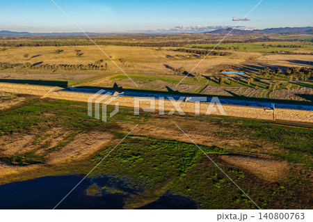 Aerial view showcasing the Lake Keepit earth embankment and surrounding rural landscape, highlighting the scale of the reservoir and the engineering features of the dam in NSW, Australia. Aerial view showcasing the Lake Keepit earth embankment and surrounding rural landscape, highlighting the scale of the reservoir and the engineering features of the dam in NSW, Australia. 140800763