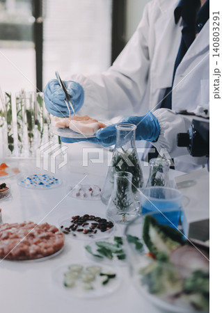 Scientists in lab coats work with plants in a modern lab, focusing on research and experimentation under bright, sterile conditions. Scientists in lab coats work with plants in a modern lab, focusing on research and experimentation under bright, sterile conditions. 140803291