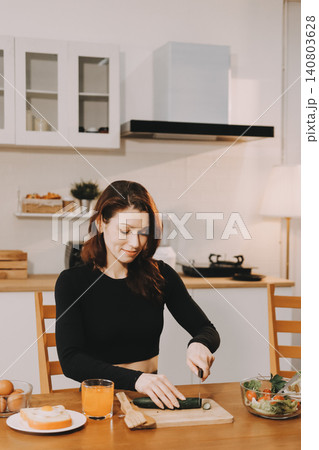 Woman preparing green smoothie in bright kitchen with fresh fruits and vegetables, healthy eating lifestyle moment in natural daylight 140803628