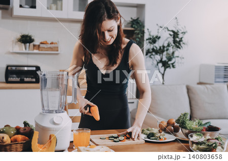 Woman preparing green smoothie in bright kitchen with fresh fruits and vegetables, healthy eating lifestyle moment in natural daylight 140803658