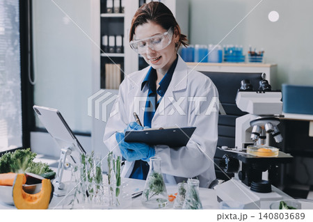 Scientists in lab coats work with plants in a modern lab, focusing on research and experimentation under bright, sterile conditions. 140803689