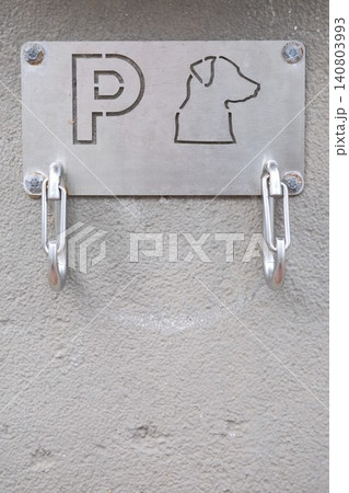 Metal carabiners or clips for attaching dog's leash at pet parking station with cutout dog sign on it. Safe leaving pets waiting area by the building wall 140803993