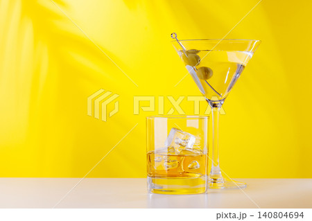Glass of whiskey with ice and martini with olives on yellow background Glass of whiskey with ice and martini with olives on yellow background 140804694
