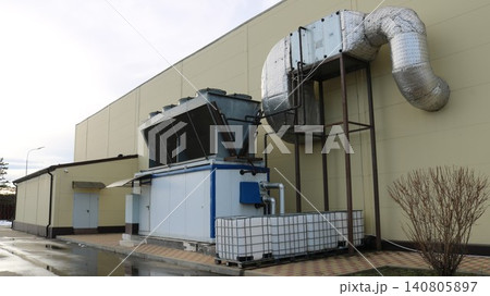 A large-scale industrial air conditioning unit, located outdoors, close to the building's blank wall. In the foreground is the main process station a single-block chiller A large-scale industrial air conditioning unit, located outdoors, close to the building's blank wall. In the foreground is the main process station a single-block chiller 140805897