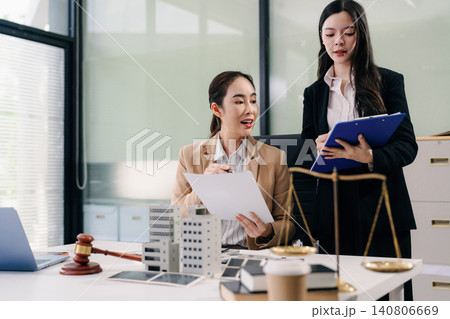 Two Asian women lawyers review real estate contracts with a model house, property law, investment, legal advice, and consultation concepts. Two Asian women lawyers review real estate contracts with a model house, property law, investment, legal advice, and consultation concepts. 140806669