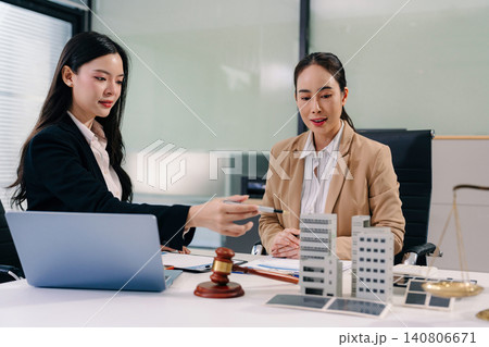 Two Asian women lawyers review real estate contracts with a model house, property law, investment, legal advice, and consultation concepts. 140806671