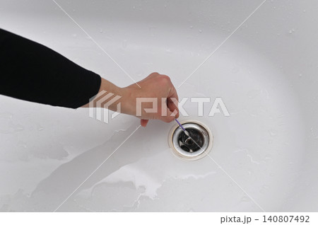 Hand extracts dirty clog from bathroom drain with plastic tool. Unclean mass of hair comes out of messy water drainage pipe. 140807492