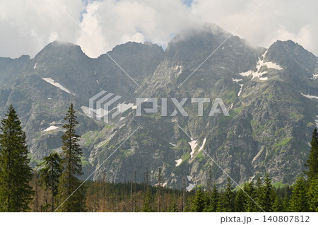 Mountain landscape with rocky peaks and forest in foreground. montane range rising under dramatic clouds. Mountain scenery shows snow patches on slopes, natural summer background, travel concept, Mountain landscape with rocky peaks and forest in foreground. montane range rising under dramatic clouds. Mountain scenery shows snow patches on slopes, natural summer background, travel concept, 140807812