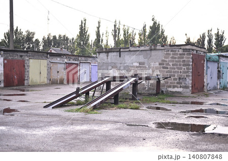 Grungy garage row looks desolated in Eastern Europe city. Metal car ramp structure serves for DIY auto service. Dilapidated property, block storage units and vintage architecture. Grungy garage row looks desolated in Eastern Europe city. Metal car ramp structure serves for DIY auto service. Dilapidated property, block storage units and vintage architecture. 140807848