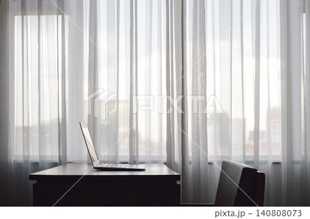 a notebook put on the wood table beside of the large window with curtain with nobody in the room of hotel or office in big city 140808073