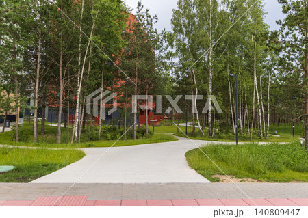 Modern bright red multi-story apartment building with geometric balconies nestled next to a green public park and pedestrian walkway. Modern bright red multi-story apartment building with geometric balconies nestled next to a green public park and pedestrian walkway. 140809447