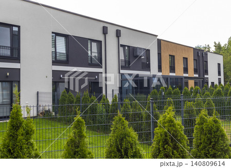 Modern minimalist townhouses with private backyards, dark metal fencing, and decorative green thuja hedge landscaping. Modern minimalist townhouses with private backyards, dark metal fencing, and decorative green thuja hedge landscaping. 140809614
