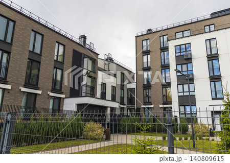 Modern residential courtyard with multi-story brick apartment buildings, minimalist facades, and a fenced green lawn space. 140809615