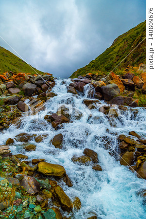 Mountain Stream Cascading Over Rocks with Green Slopes Mountain Stream Cascading Over Rocks with Green Slopes 140809676