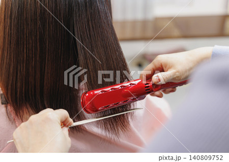 赤いヘアアイロンとコームで女性の髪をストレートにする 赤いヘアアイロンとコームで女性の髪をストレートにする 140809752