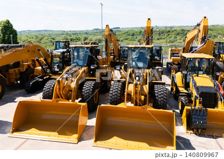New hydraulic excavators and tractors parked at a construction machinery dealership. New hydraulic excavators and tractors parked at a construction machinery dealership. 140809967