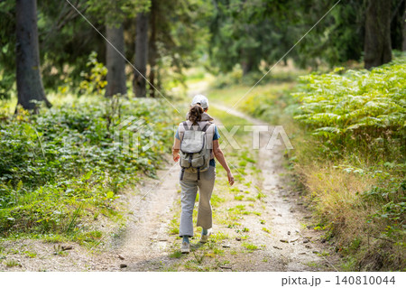 Female hiker with a backpack walking along a scenic forest road Female hiker with a backpack walking along a scenic forest road 140810044