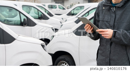 Fleet manager with digital tablet supervising rows of white delivery vans.. 140810176