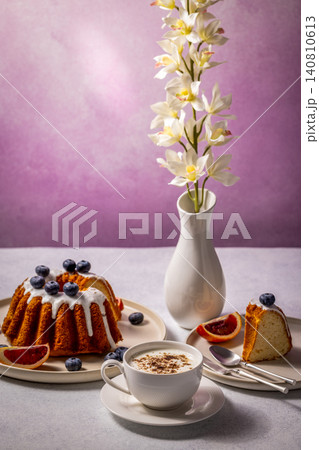 Delicious gugelhupf cake with icing, blueberries and coffee enjoyed on table decorated with orchids Delicious gugelhupf cake with icing, blueberries and coffee enjoyed on table decorated with orchids 140810613