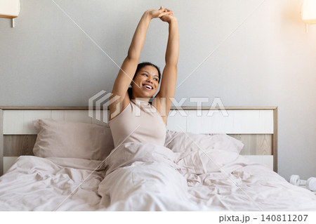 Happy black woman is stretching in bed after waking up Happy black woman is stretching in bed after waking up 140811207