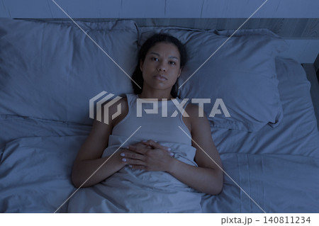 Black woman lying awake in bed at night with serious expression Black woman lying awake in bed at night with serious expression 140811234